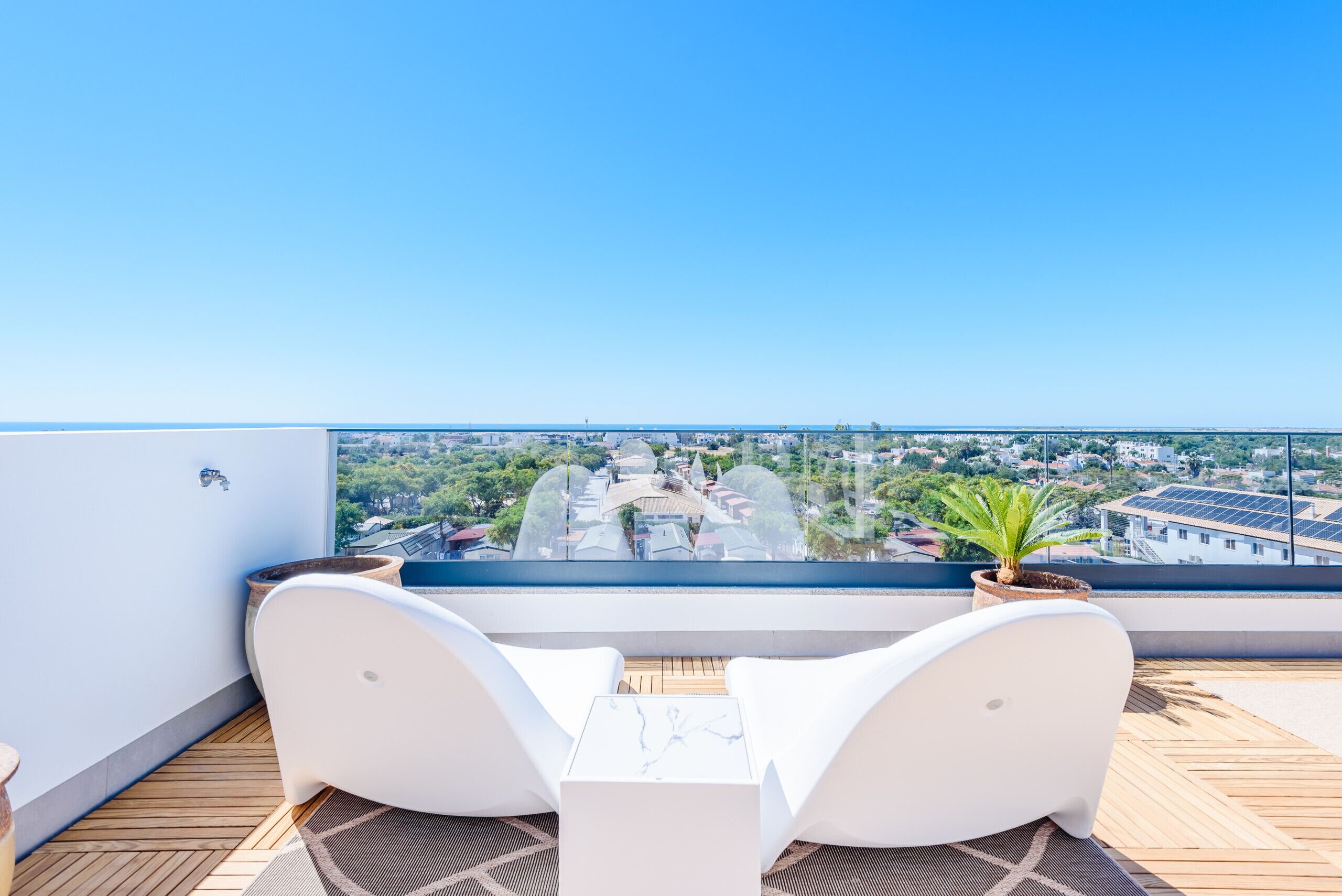 Un balcon avec deux chaises blanches et une petite table, donnant sur un paysage urbain.
