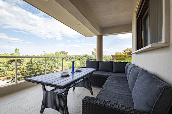 A balcony with a table and seating, overlooking a garden.