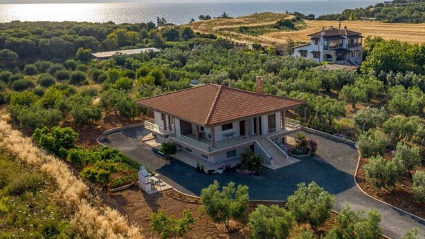 Ein großes Haus mit Ziegeldach, umgeben von Grün und Blick auf das Meer.