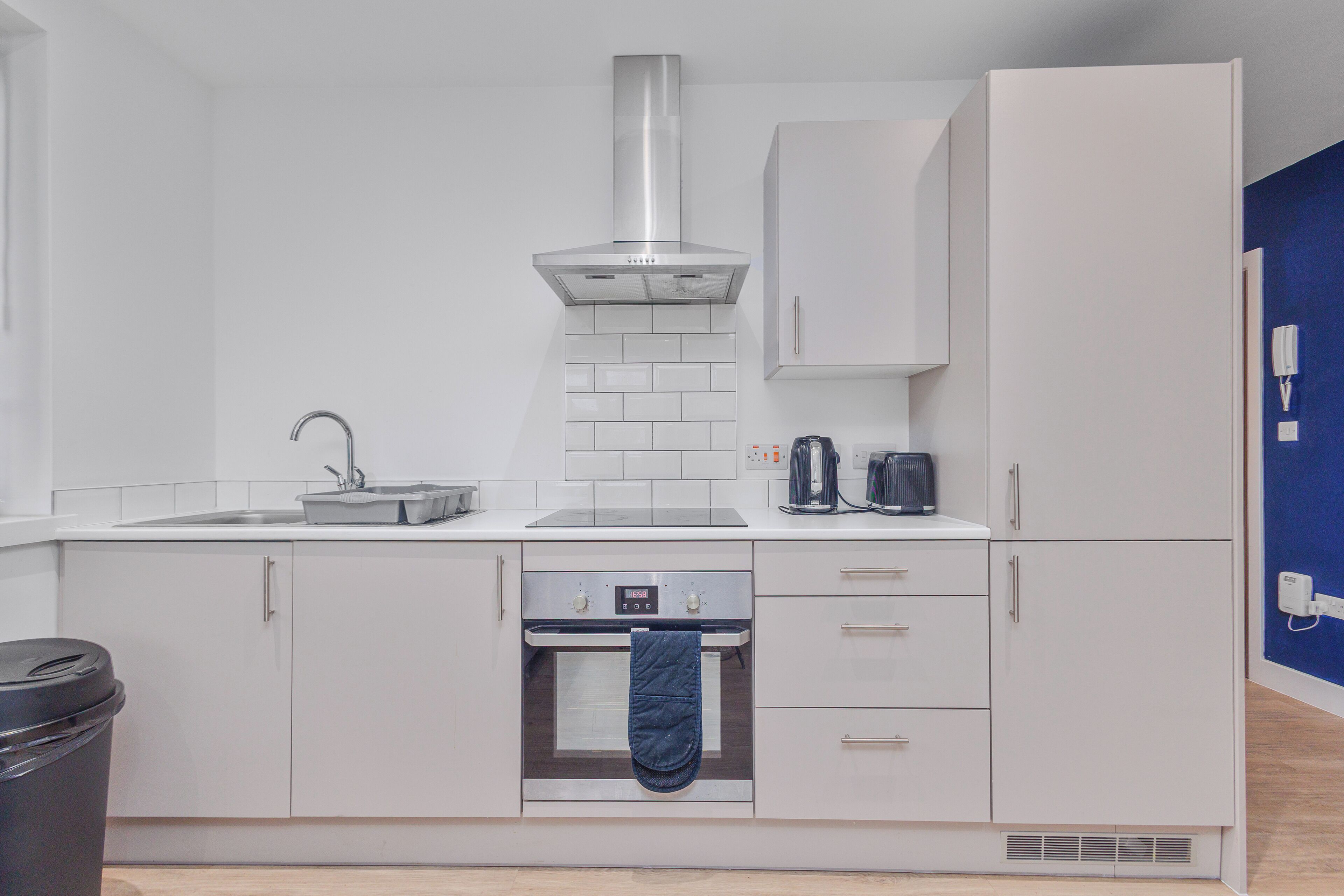 A modern kitchen with white cabinetry, a stainless steel range hood, a built-in oven, and a coffee maker.