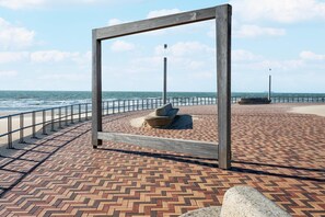 Une promenade dallée, agrémentée d’une rambarde en métal, d’un banc en pierre et d’une structure en bois.