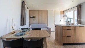 A modern kitchen with wooden cabinets, a dining area with a table set for two, and a grey sofa in the background.