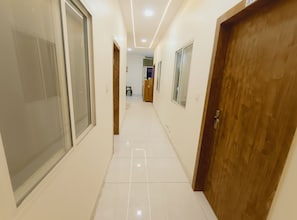 A hallway with white walls, a tiled floor, and wooden doors. - Hotel Shree Sanwariya Inn (Ujjain)