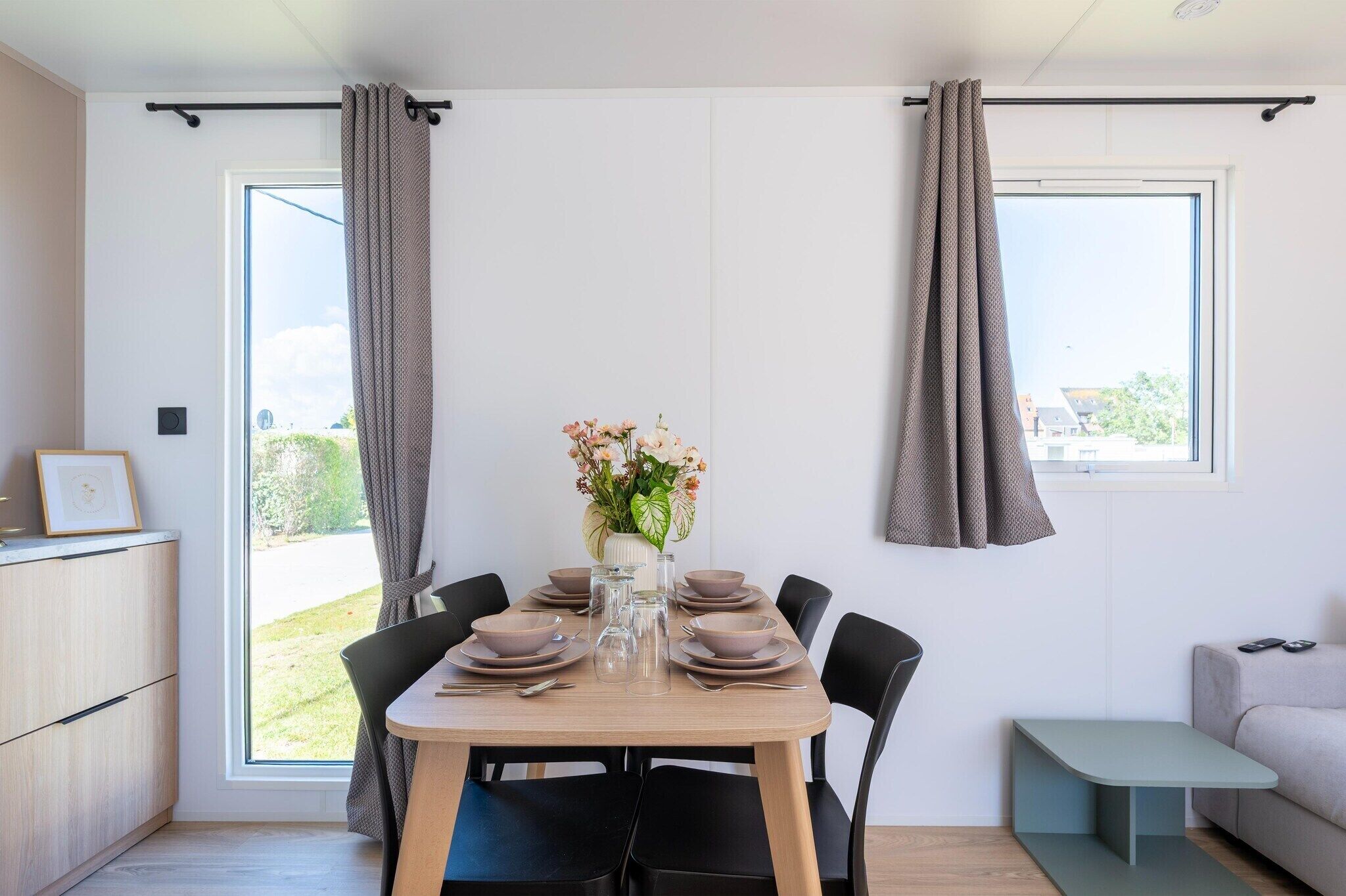 Ein Essbereich mit Tisch für vier Personen, einer Blumenvase und Blick durch das Fenster.