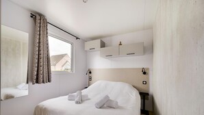 A bedroom with a bed, a mirror, a window with curtains, built-in shelves, and a bedside table.