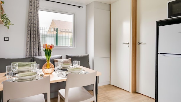 A compact kitchen with a dining area, a refrigerator, and a window with curtains.