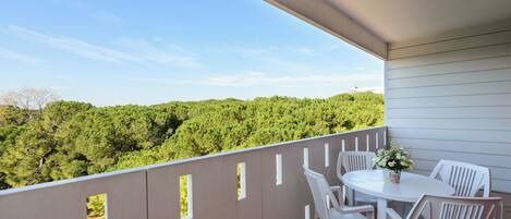 A balcony with a view of a forest, a round table with chairs, and a vase of flowers.