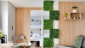 Ein modernes Zimmer mit Essbereich, einem Bett und einer Wohnbereits mit einer Couch sowie einer dekorativen Pflanzenwand.