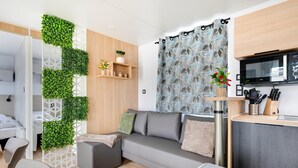 Ein modernes Wohnzimmer mit grauem Sofa, einem kleinen Tisch und einer Küchenzeile mit einer Mikrowelle.