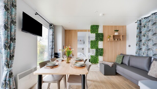 Ein modernes Wohnzimmer mit Essbereich, Flachbildfernseher, einer Couch und einer Wandgestaltung in Grün.
