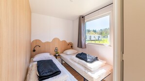 Quarto com duas camas, uma janela com cortinas, uma mesinha com uma planta e vista para um parque.