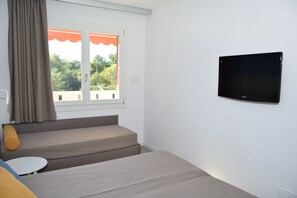 Een kamer met een bed, een klein tafeltje, een aan de muur bevestigde televisie en een raam met gordijnen.