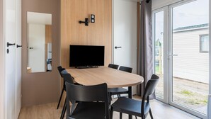 Una habitación moderna con una mesa redonda, sillas negras, un televisor de pantalla plana y una puerta corrediza de vidrio al exterior.