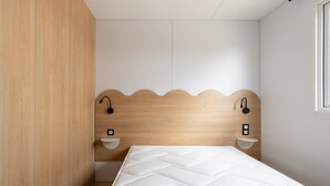 Un dormitorio con cabecera de madera, colchón blanco y dos mesitas de noche con lámparas de pared.