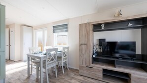 Ein modernes Wohnzimmer mit Essbereich, Holzboden, einem Flachbildfernseher und einer hellen Wand.