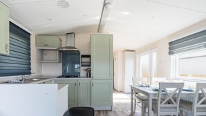 Eine kompakte Küche mit Spüle, Herd und Schränken, ein Essbereich mit Tisch und Stühlen sowie ein Fenster mit Jalousien.