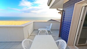 Un balcone con tavolo e sedie bianche, vista sulla spiaggia e un muro con piastrelle azzurre.