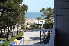 Blick auf einen Strand mit Sonnenschirmen und Liegestühlen, eine Straße, die zum Strand führt, und ein Geschwindigkeitsbegrenzungsschild.
