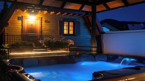 Une cabane en bois avec un jacuzzi, une véranda avec des marches et une entrée éclairée.