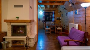 Un intérieur de chalet chaleureux avec une cheminée, des murs en bois, un coin repas et un canapé violet.