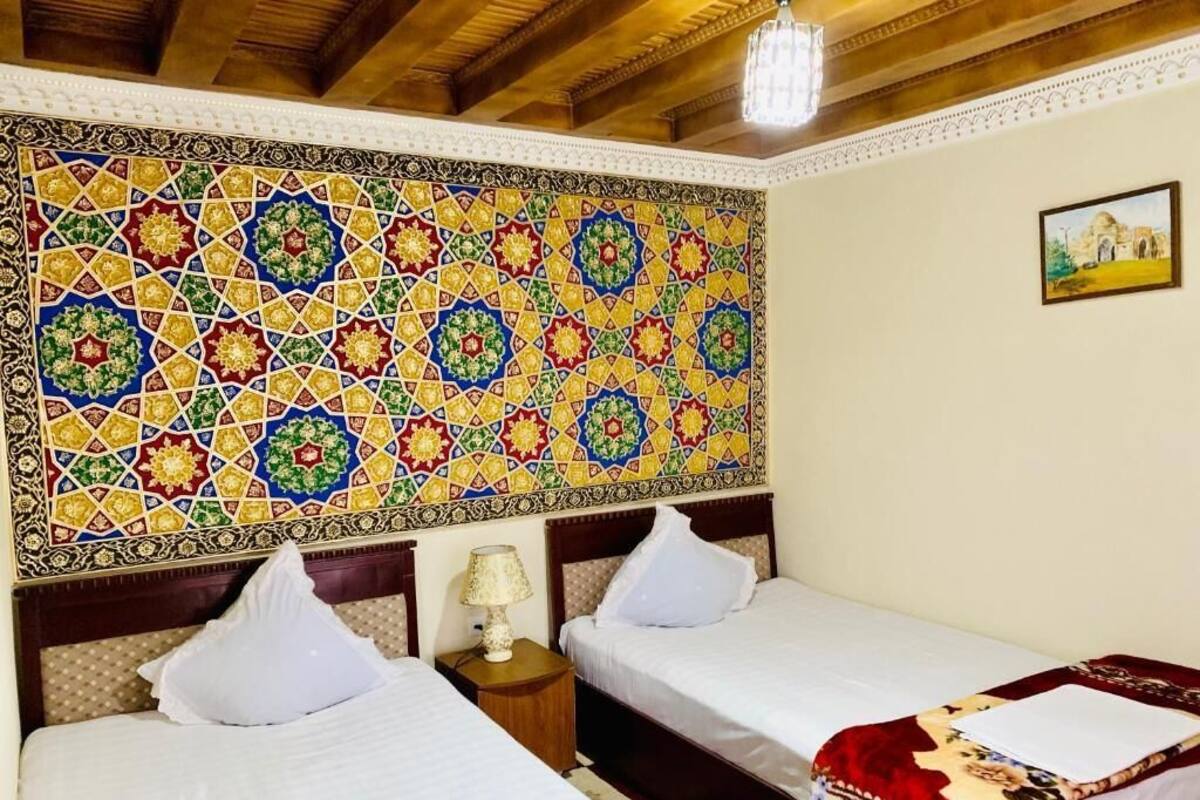 Una habitación con dos camas, un papel tapiz estampado, una araña y un cuadro en la pared.