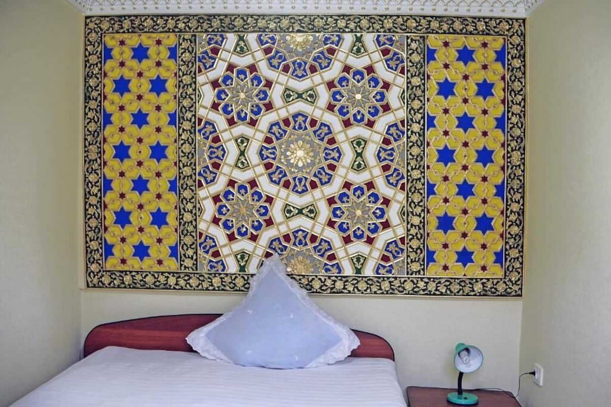 Una habitación con una cama, un tapiz en la pared y una mesita de noche con lámpara.