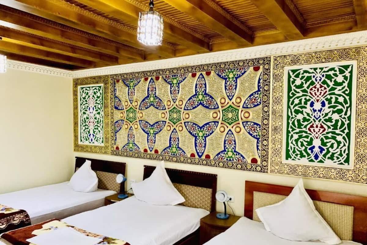 Habitación de hotel con tres camas, cabeceros de madera y diseños decorativos en la pared.