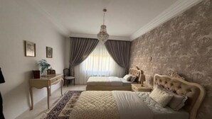 Quarto com duas camas, um candelabro, uma escrivaninha e parede estampada.