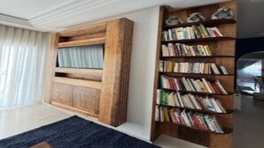 Quarto com estante, janela com cortinas e tapete azul escuro.