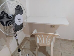 A standing fan with a label, a white chair, and a white shelf unit in a room with tiled flooring.