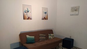 A living room with a brown sofa, three cushions, two wall-mounted artworks, and a patterned rug. - 001 - Apartment Close to the Center (Vitoria da Conquista)