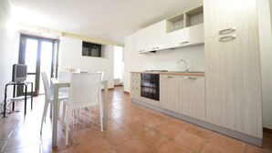 A modern kitchen with white cabinets, a black oven, and a dining area with a white table and chairs. - VACATION HOME " THE BELVEDERE ON THE STONES " CIN: IT077014C202430001 (Matera)