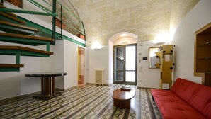 A room with a patterned floor, a red sofa, a small round table, a staircase with green railings, and a door with a mirror. - VACATION HOME " THE BELVEDERE ON THE STONES " CIN: IT077014C202430001 (Matera)