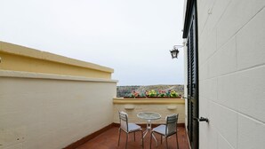 A small outdoor patio with a table and two chairs, a flower box with colorful flowers, and a view of a hilly landscape. - VACATION HOME " THE BELVEDERE ON THE STONES " CIN: IT077014C202430001 (Matera)
