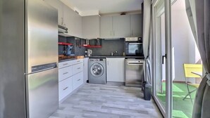 Cocina compacta con lavadora, horno y vista a un espacio exterior verde.