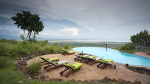 A pool with lounge chairs, a view of the landscape, and a cloudy sky. - Lake Manyara Serena Safari Lodge (Lake Manyara National Park)