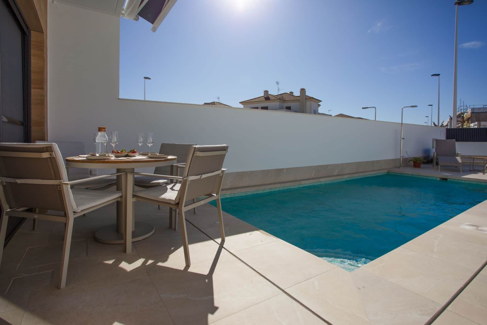 Ein Poolbereich mit Tisch und Stühlen, einem klaren blauen Pool und einer weißen Wand.
