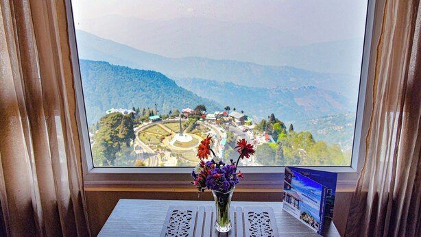 A window view of a mountainous landscape with a table and a vase of flowers. - Anutri Hotels & Resorts  (Darjeeling)