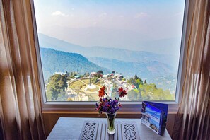 Une vue par la fenêtre sur un paysage montagneux, avec une table et un vase de fleurs.