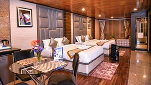 A hotel room with a wooden ceiling, a large bed with a headboard, a dining table with chairs, and a small table with a vase of flowers. - Anutri Hotels & Resorts  (Darjeeling)