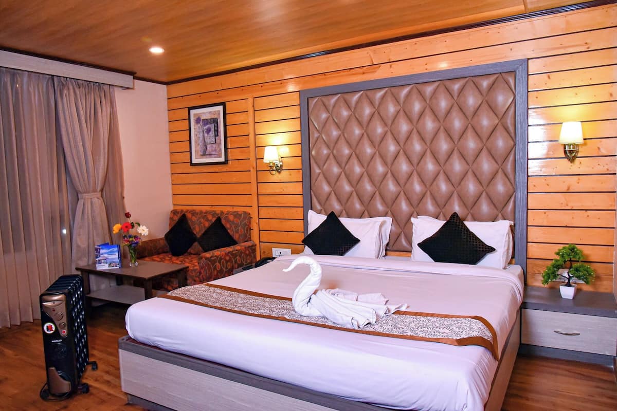 A hotel room with a bed, a sofa, a desk with a lamp, a small plant, and a wall-mounted picture.