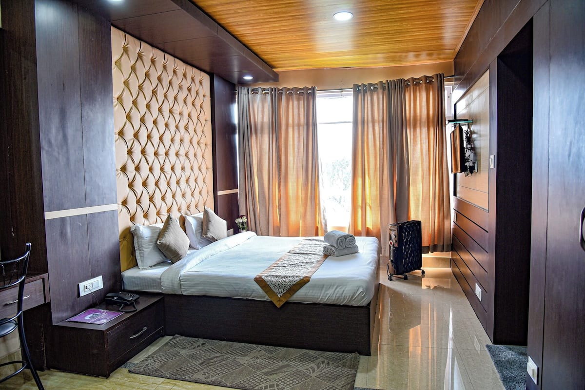 A bedroom with a large bed, a headboard with a geometric pattern, a bedside table with a lamp, and a window with curtains.