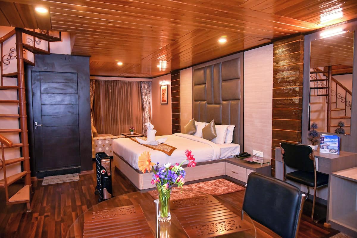 A hotel room with a wooden ceiling, a bed with a headboard, a desk with a chair, and a small table with a vase of flowers.