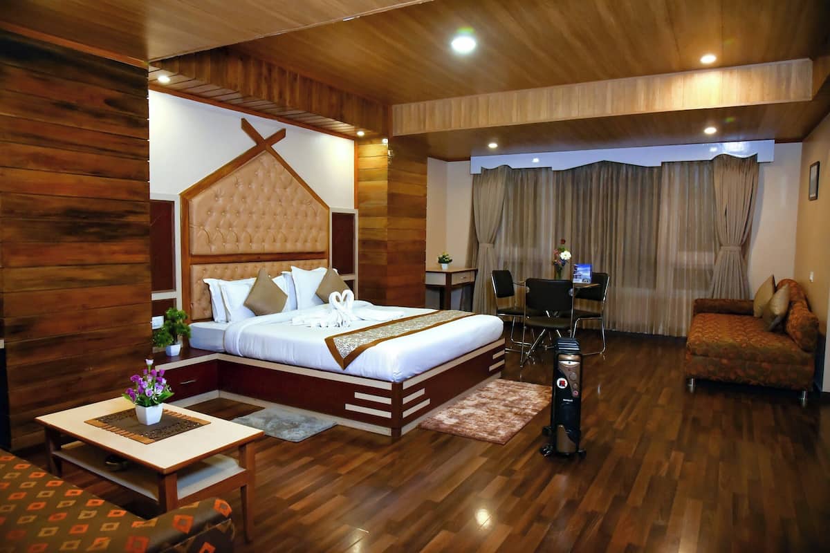 A hotel room with a wooden floor, a bed with a headboard, a desk with a chair, a sofa, and a small table with a plant.