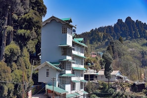 Un immeuble à plusieurs étages, de style architectural traditionnel, entouré d’une forêt dense et de montagnes.