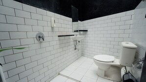 Un baño pequeño con azulejos blancos, que incluye un inodoro, lavamanos y secamanos.