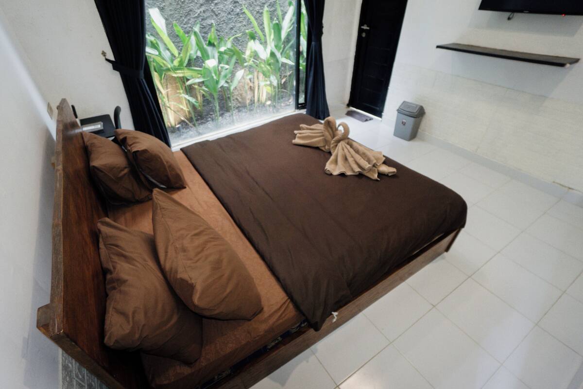 A bed with brown bedding, a wooden headboard, and a window with a view of plants.