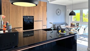 Una cocina moderna con una isla negra, armarios de madera, horno empotrado y un amplio ventanal.