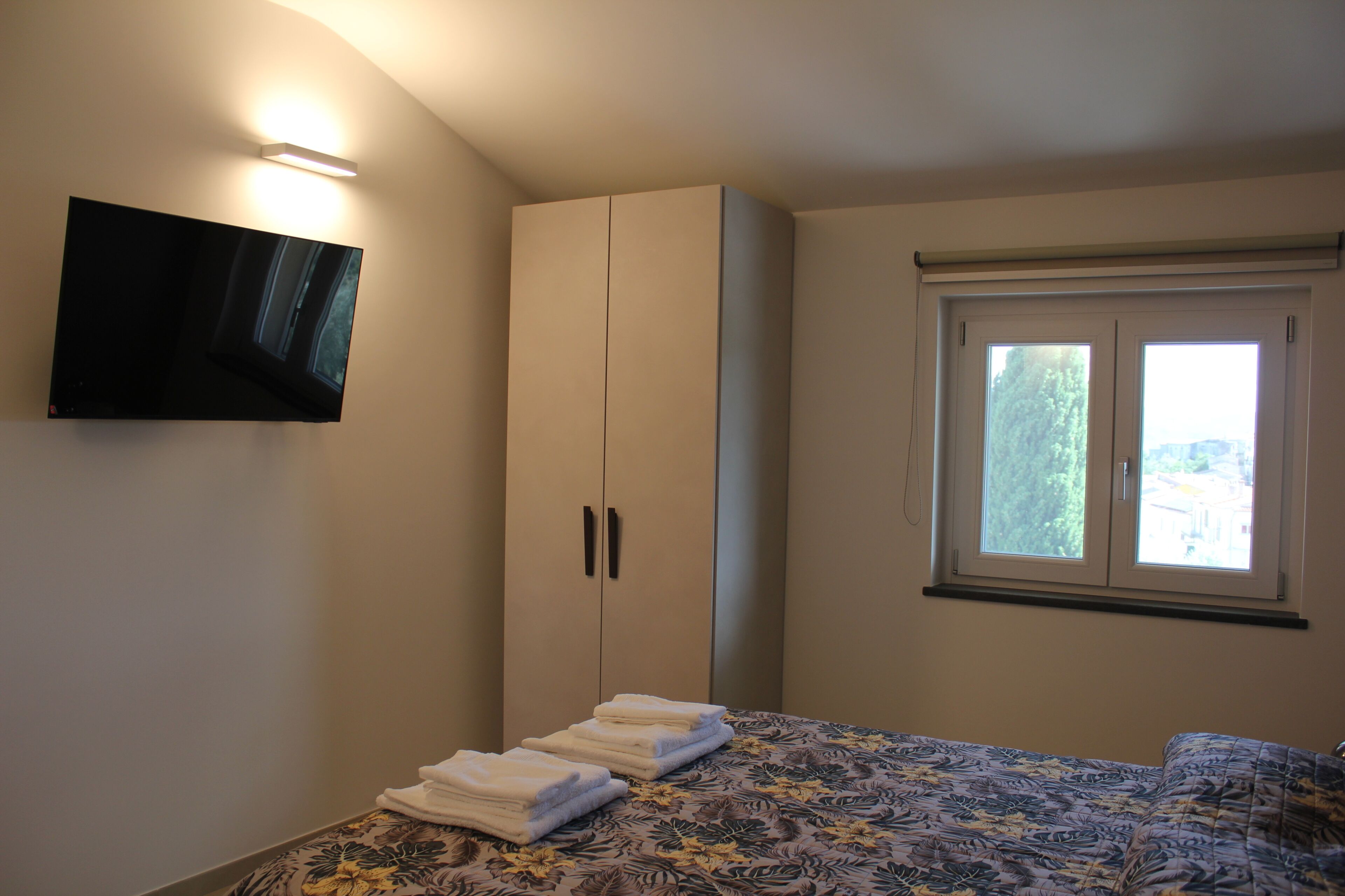 Ein Schlafzimmer mit einem Bett, einem Kleiderschrank, einem Flachbildfernseher und einem Fenster.