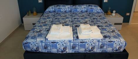 Una cama bien hecha con un edredón estampado, dos mesitas de noche con lámparas y un banco de color oscuro.